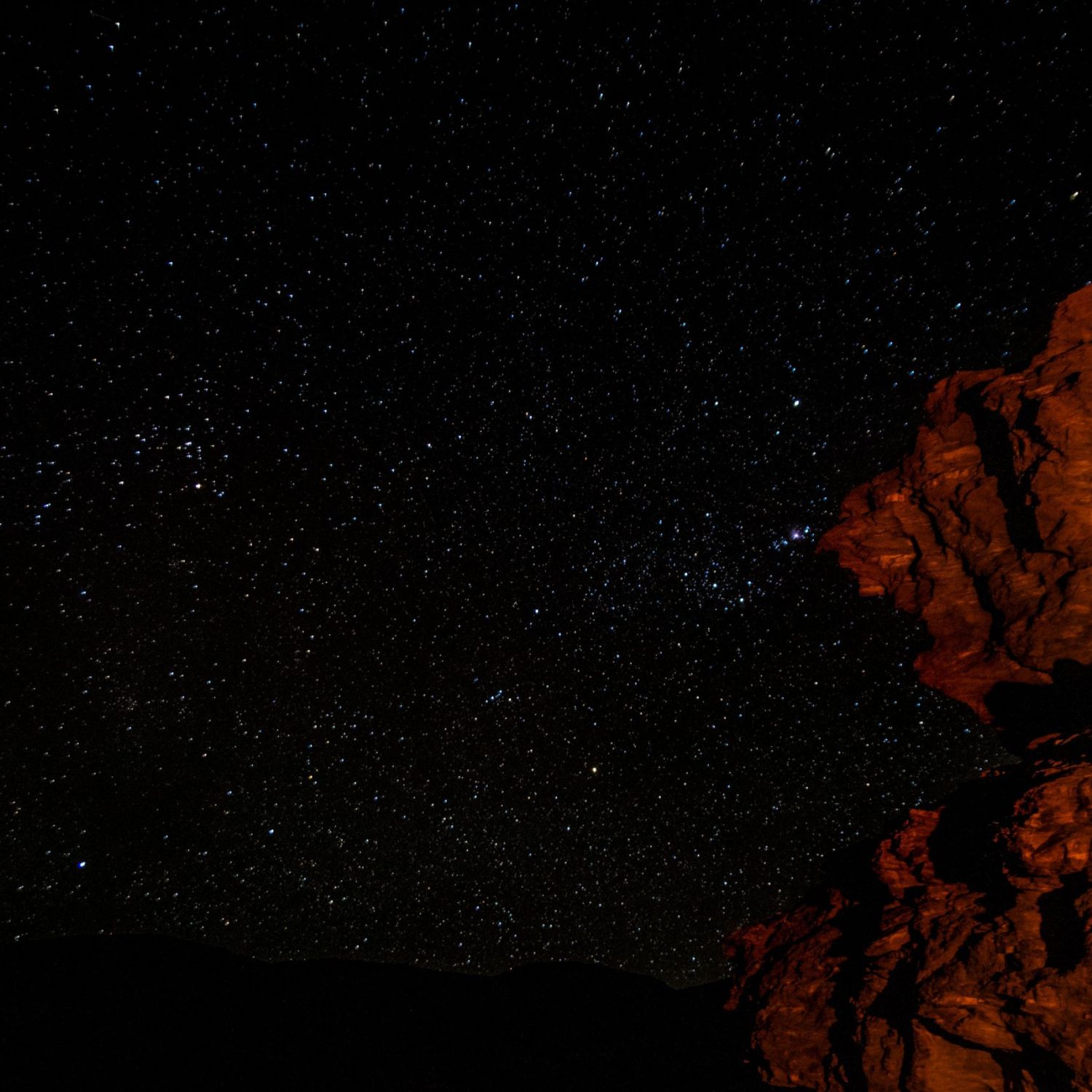 Sternenhimmel mit von Lagerfeuer beleuchtetem Fels im Vordergrund